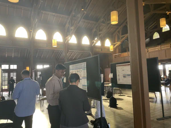 Attendees walking among research posters under tall hall windows.