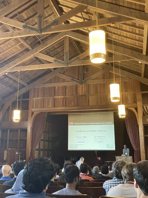 A speaker presents research slides to an audience in the conference hall.